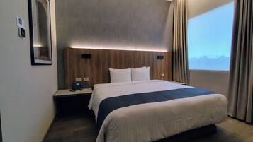Habitación de hotel moderna con una cama grande, una mesita de noche con teléfono y vista a la ciudad por la ventana.