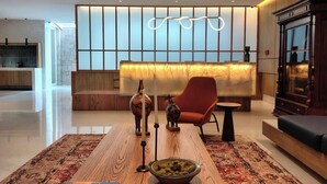 Een moderne lobby met een receptiebalie, een zithoek met een rode stoel, een houten bijzettafeltje en een decoratieve vaas.