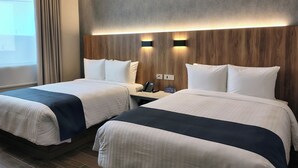 Een hotelkamer met twee bedden, een houten hoofdbord, nachtkastjes met lampen, en uitzicht buiten.