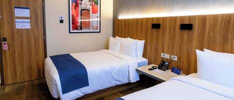 A hotel room with two beds, a wooden headboard, a nightstand with a phone, and a framed picture on the wall.