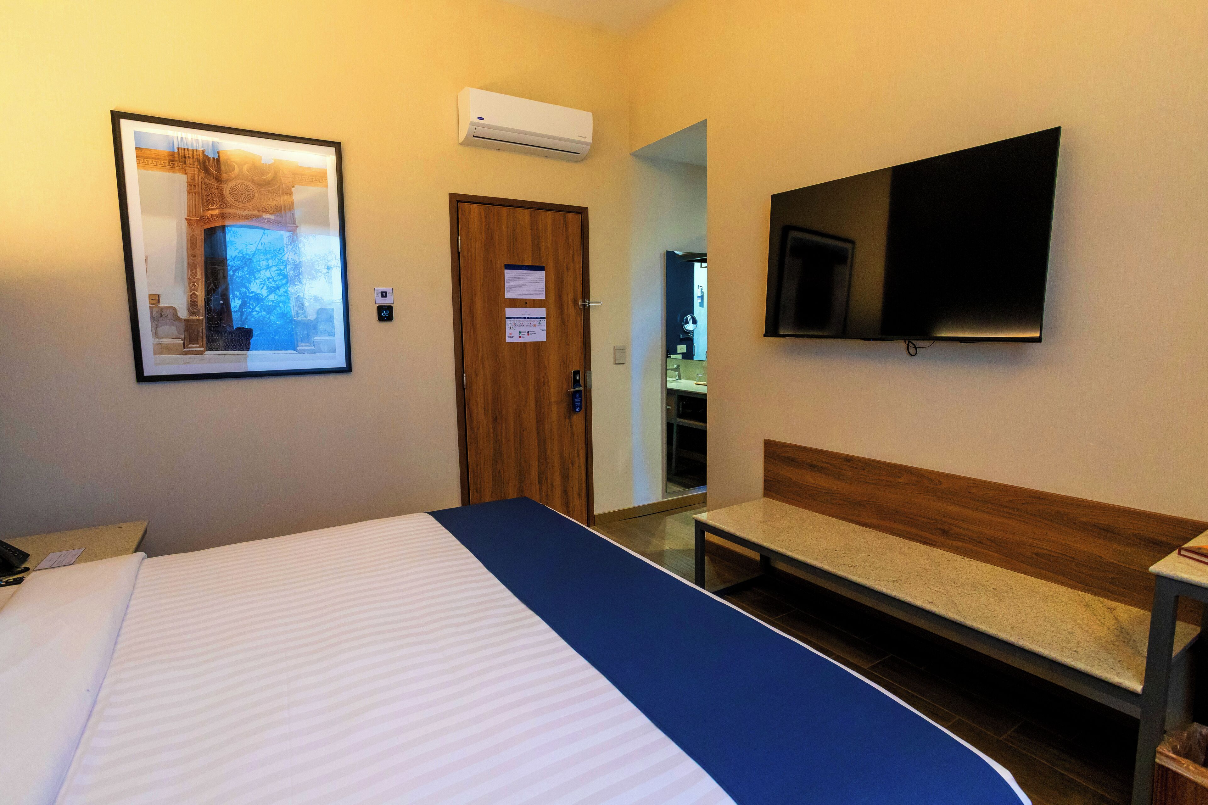 Una habitación de hotel con una cama, un banco, un televisor y una puerta.
