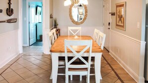 A dining room with a wooden table and white chairs, a chandelier, a mirror, and a framed picture on the wall.