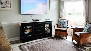 A living room with a flat-screen TV, wicker furniture, a glass cabinet, and a view through a window.