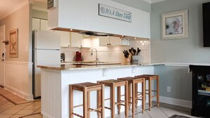 A kitchen with a central island, bar stools, a refrigerator, and a sign that reads "It's A Shore Thing".