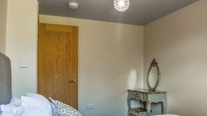 Une chambre à coucher avec un lit, une porte en bois, une commode avec un miroir et un luminaire au plafond.