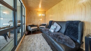 A cozy room with a leather sofa, a glass door, and a wooden ceiling. - Strathvale River Cottage - Winton Holiday Home (Winton)