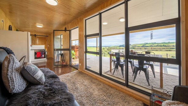 A cozy living room with a large window, a wooden ceiling, and a view of the countryside. - Strathvale River Cottage - Winton Holiday Home (Winton)