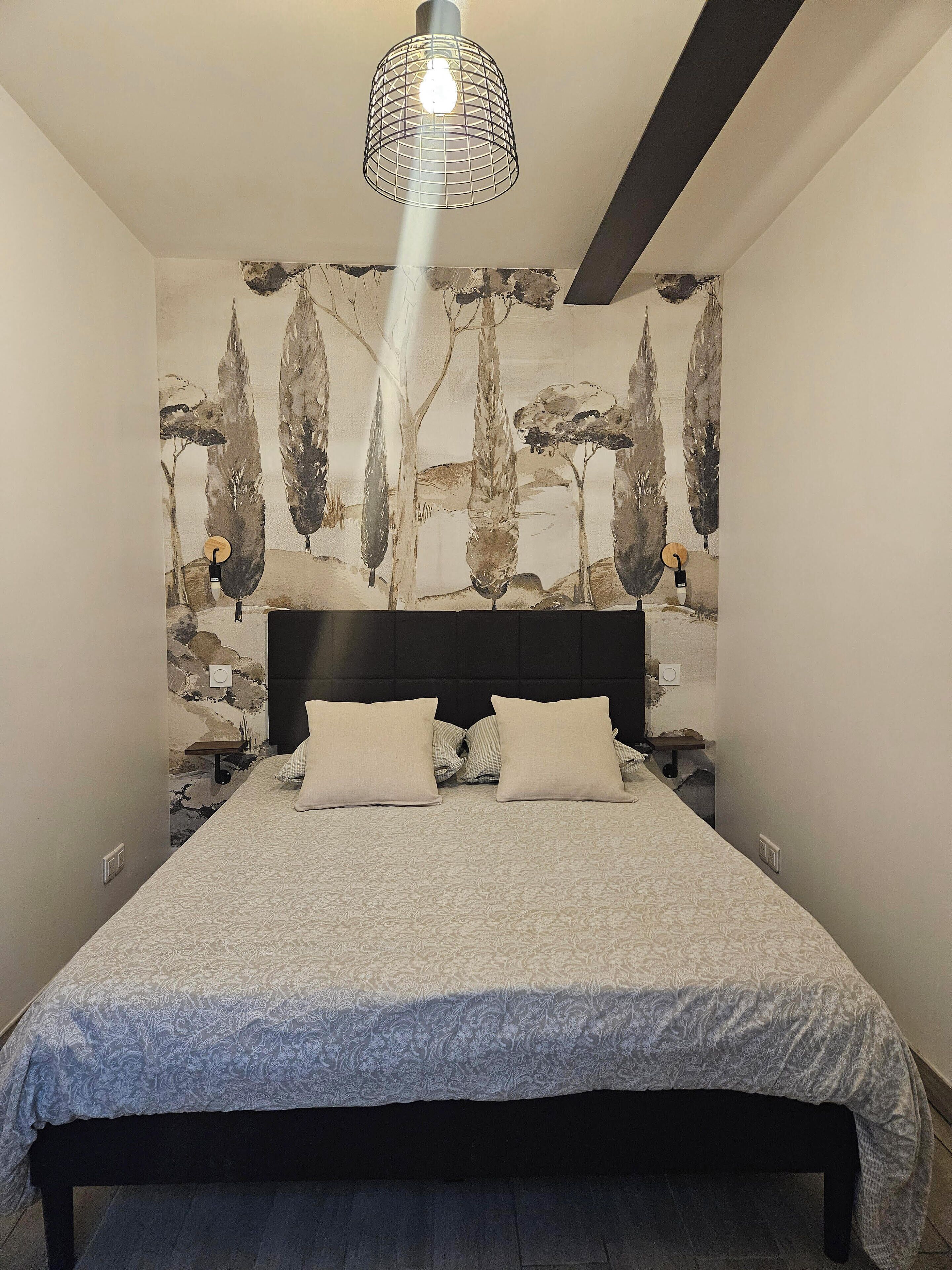 Un dormitorio con una cama, cabecera, pared con un mural temático de naturaleza y una lámpara colgante.