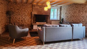 A cozy living room with a stone wall, a fireplace, a sofa, and a checkered floor. - Le Clos Loret (Saint-Germain-du-Corbéis)