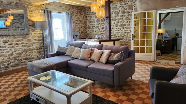 A cozy living room with a stone wall, a checkered floor, a sofa with cushions, a glass coffee table, and a wooden ceiling. - Le Clos Loret (Saint-Germain-du-Corbéis)