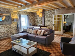 A cozy living room with a stone wall, a checkered floor, a sofa with cushions, a glass coffee table, and a wooden ceiling.