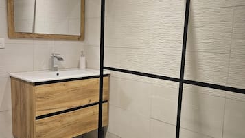 Ein modernes Badezimmer mit einem Holzkosmetikschrank, einem Spiegel und einer Duschkabine.