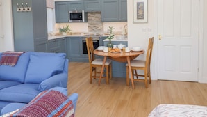 A modern kitchen with grey cabinets, a microwave, and a sink. There is a dining table with chairs and a blue sofa in the living area. - West End (Woodbridge)