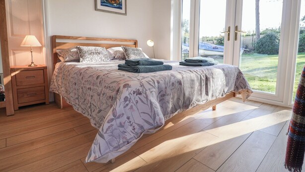 A bedroom with a bed, a nightstand, a lamp, and a view of the outdoors through a sliding door. - West End (Woodbridge)