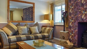 A living room with a sofa, a coffee table, a lamp, a mirror, and a floral wallpaper.
