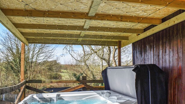 A hot tub under a wooden pergola with a view of trees and a fence.