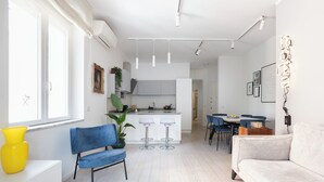 Een moderne keuken met witte kasten, een eethoek met blauwe stoelen en een lichtkleurige bank.