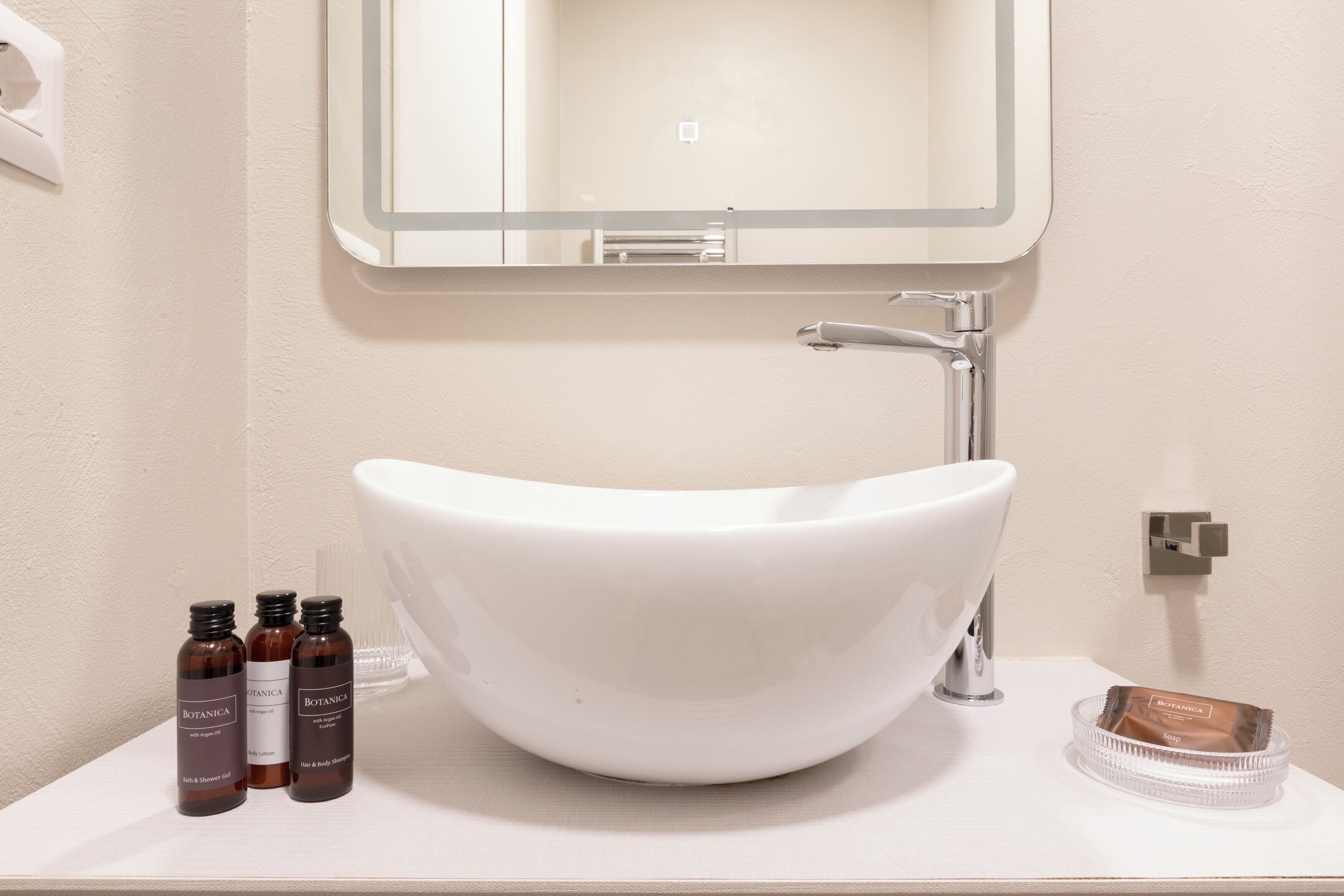 A bathroom with a white sink, a mirror, and three bottles of Botanica body wash.