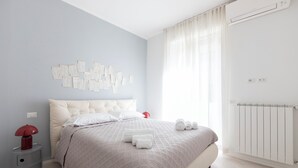 Een slaapkamer met een bed, nachtkastje, een luchtverkoeler aan de muur en een raam met gordijnen.