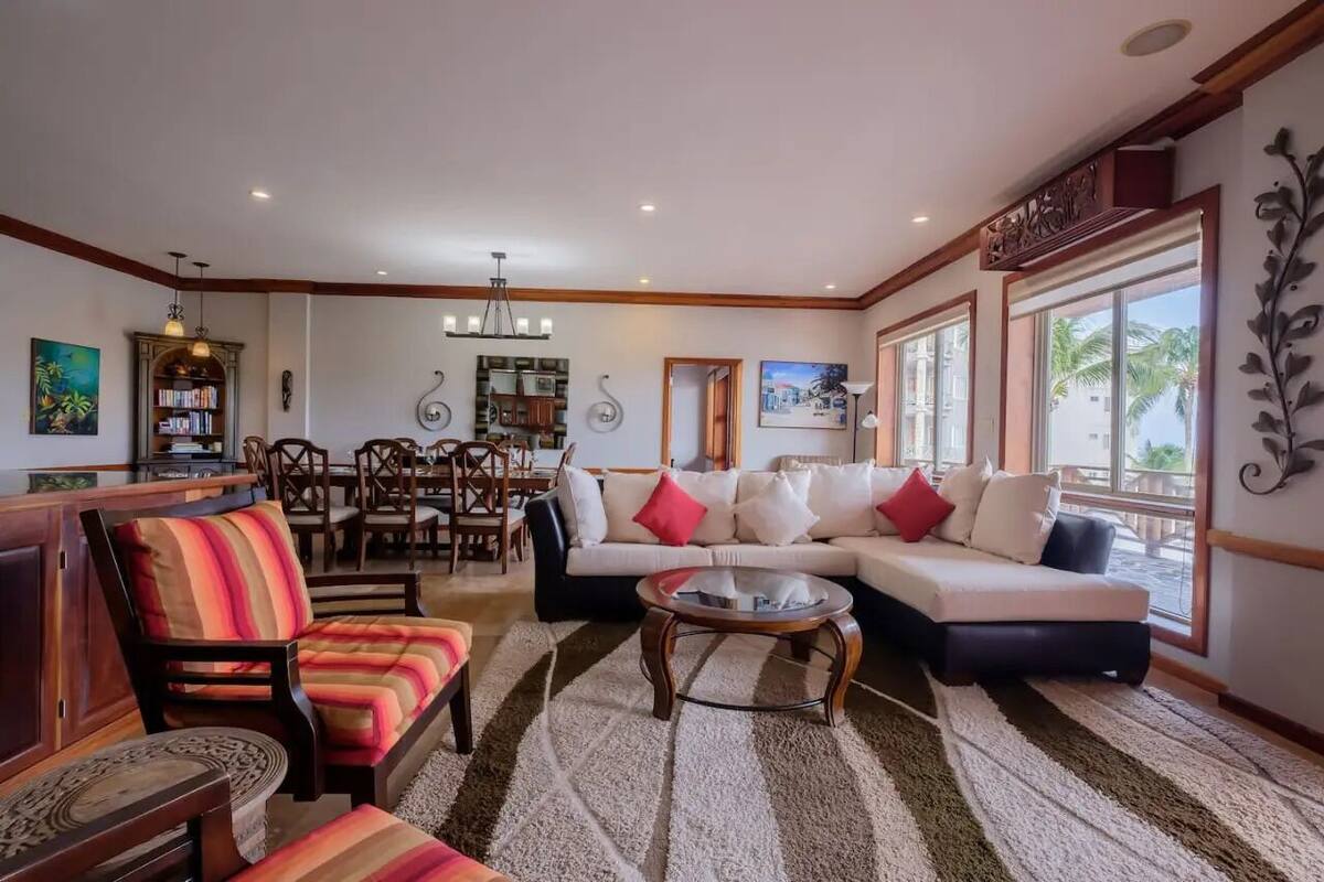 A spacious living room with a sofa, chairs, a coffee table, a dining area with a table and chairs, and a bookshelf.