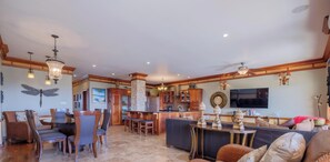 A spacious living area with a dining set, a kitchen in the background, and a large TV mounted on the wall. - Oceans 23 (San Pedro)