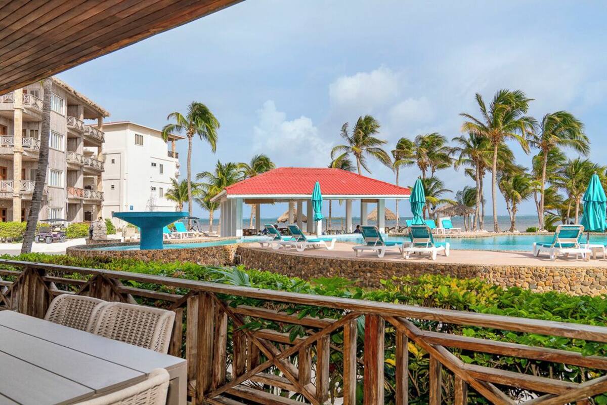 A resort pool area with lounge chairs, a central fountain, and a red-roofed pavilion.
