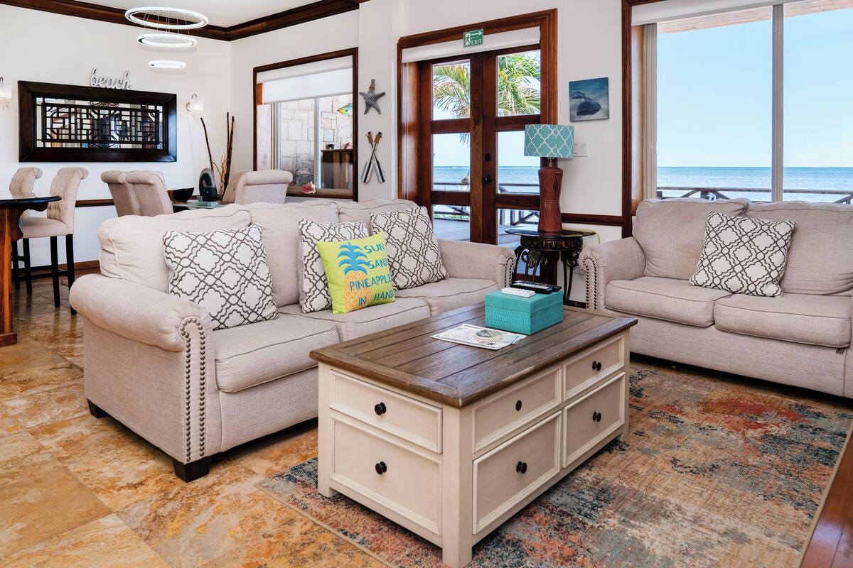 A cozy living room with a beige sofa, a wooden coffee table, and a view of the ocean through large windows.