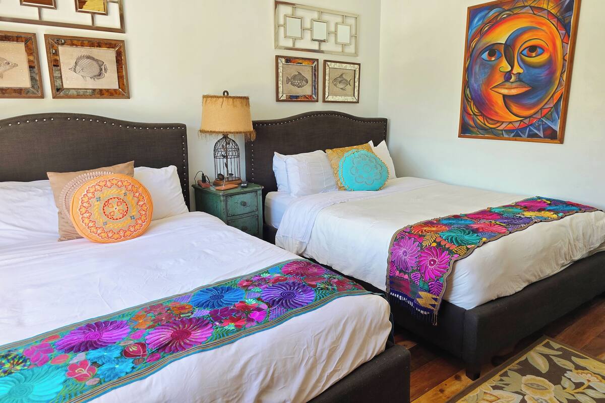A hotel room with two beds, a nightstand, a lamp, and wall art.