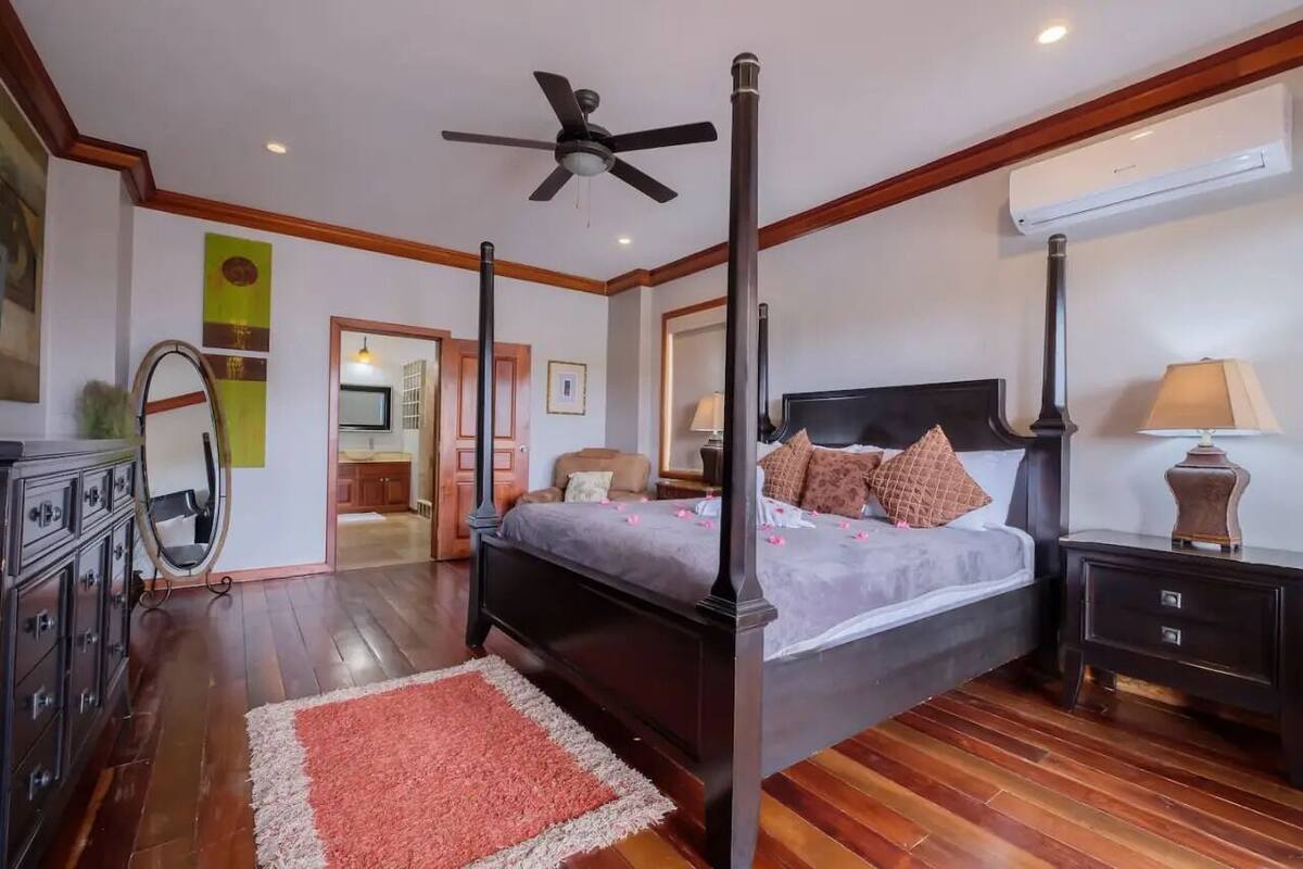 A four-poster bed with a ceiling fan, a nightstand, a dresser, and a mirror.