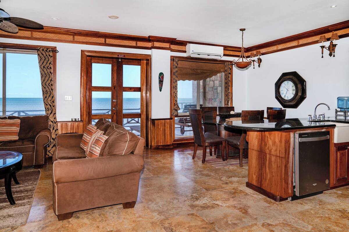 A spacious living area with a large brown sofa, a dining table, and a kitchen area with a built-in dishwasher.