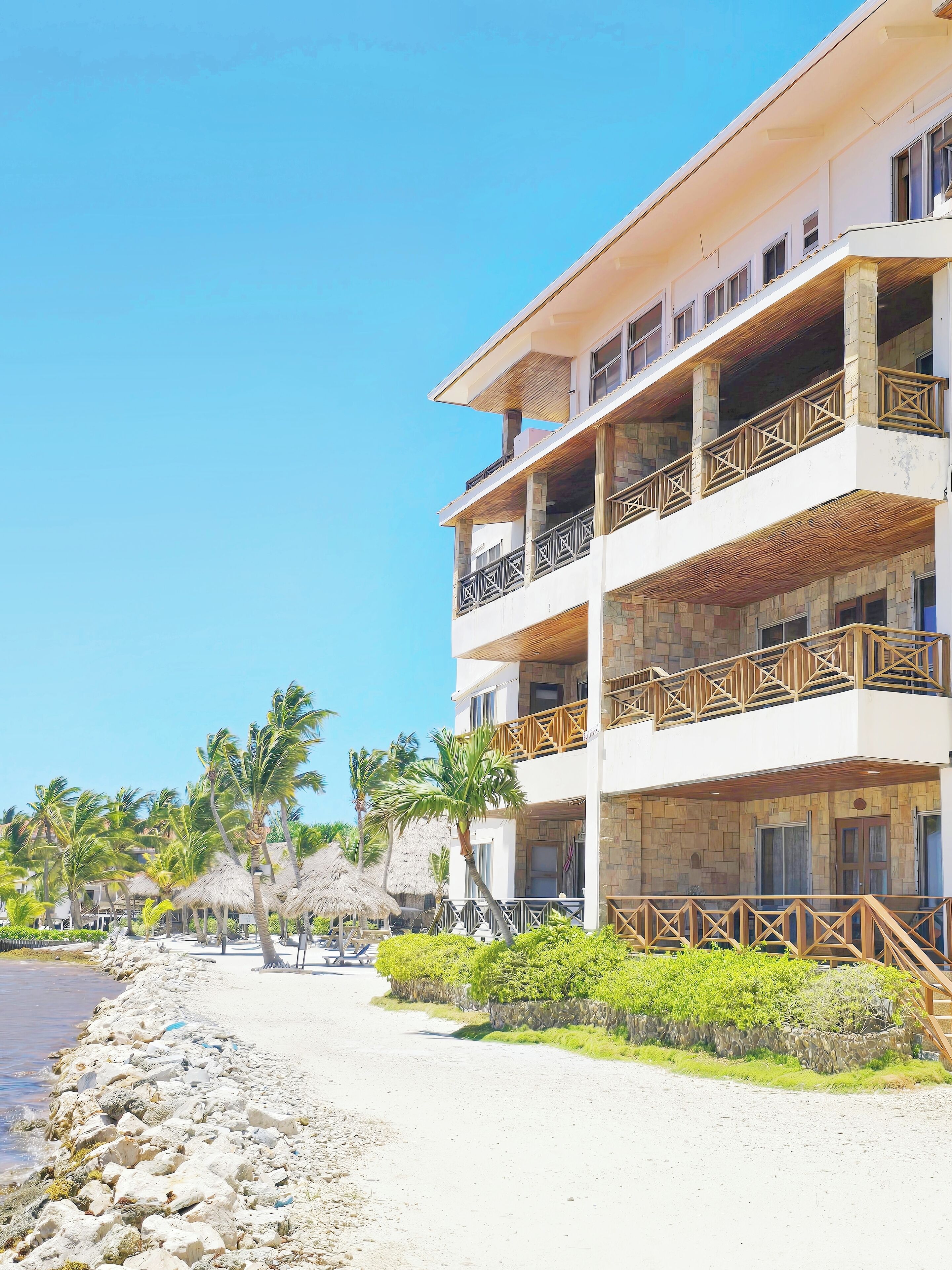 A multi-story hotel with balconies, a beachside location, and palm trees.