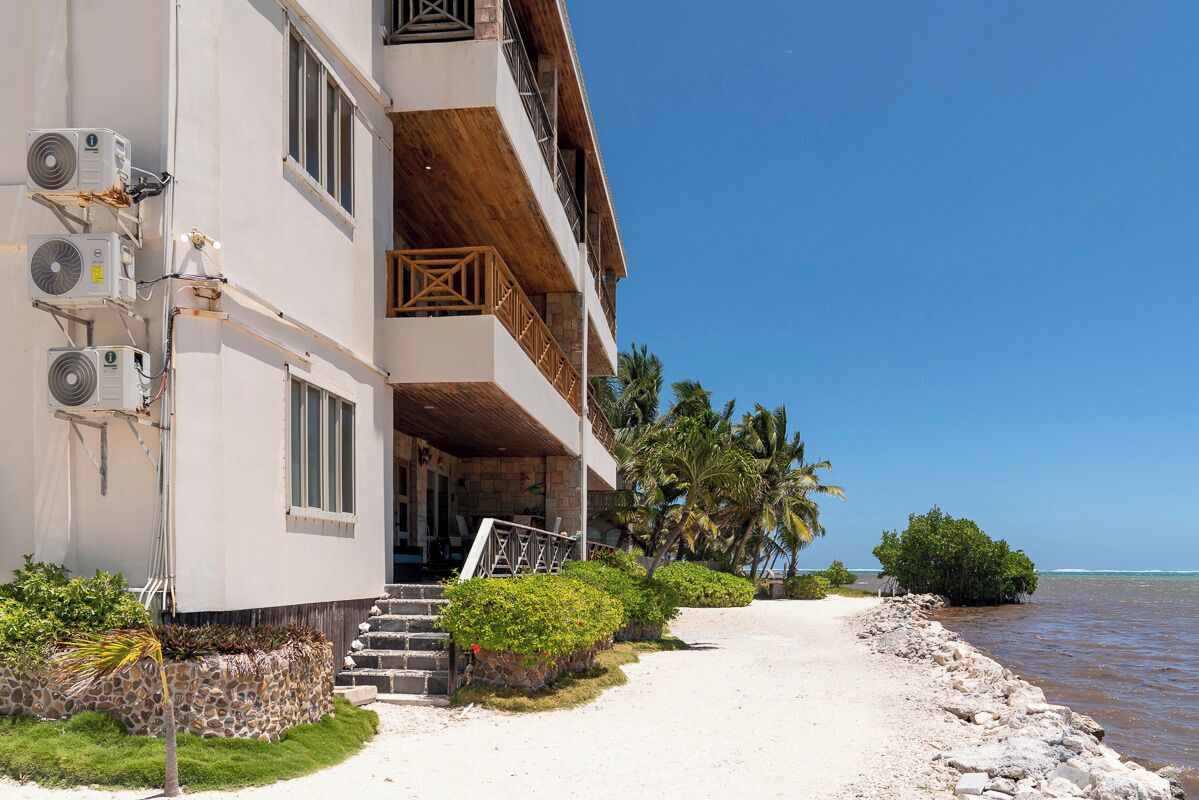 Un hotel frente a la playa con varios balcones, un paseo marítimo de arena y vista al océano.