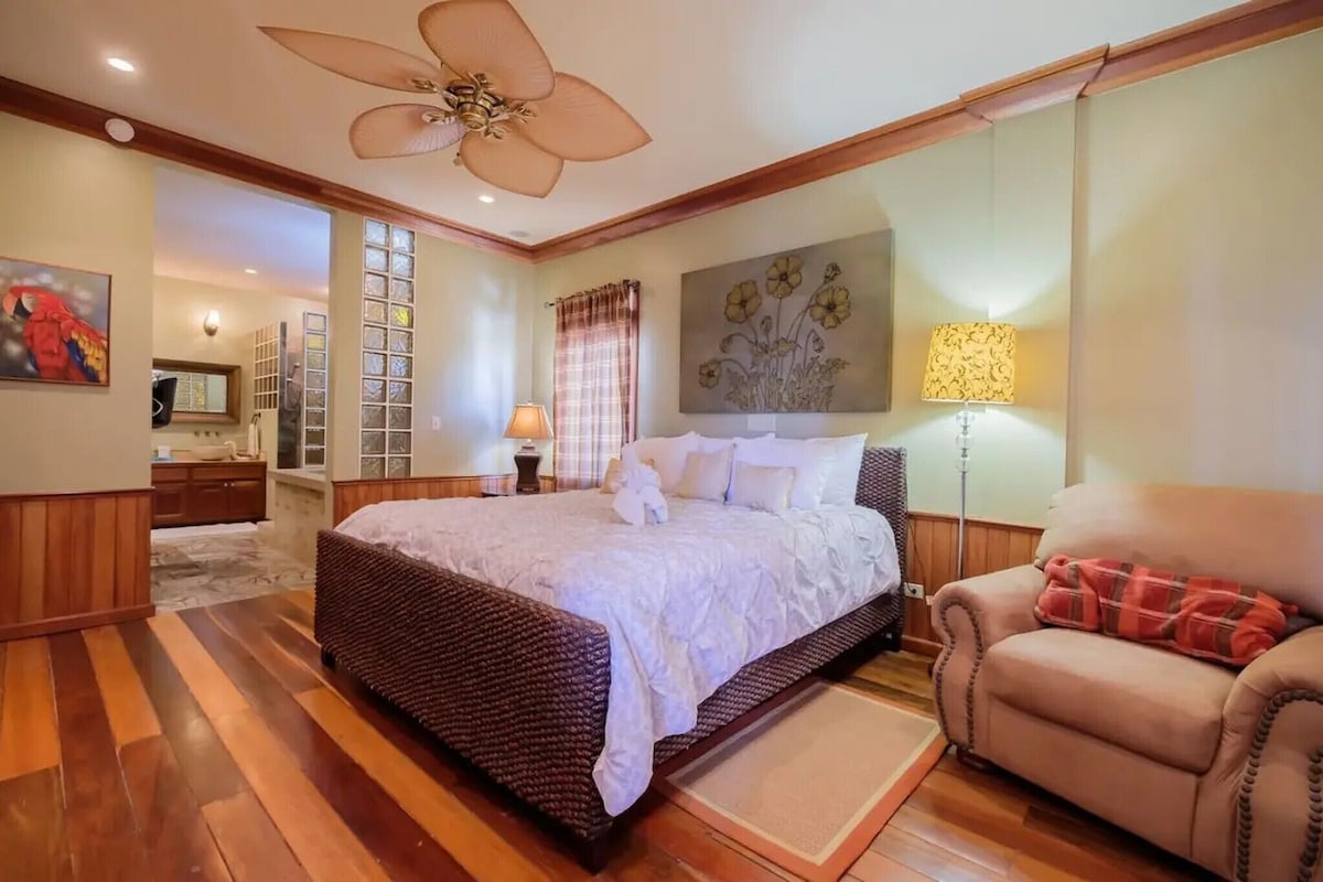 A bedroom with a large bed, a chair, a floor lamp, and a ceiling fan.