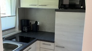 A compact kitchen with light wood cabinets, a black countertop, a sink, and a microwave. - Vacation home with Lilienstein view (Struppen)