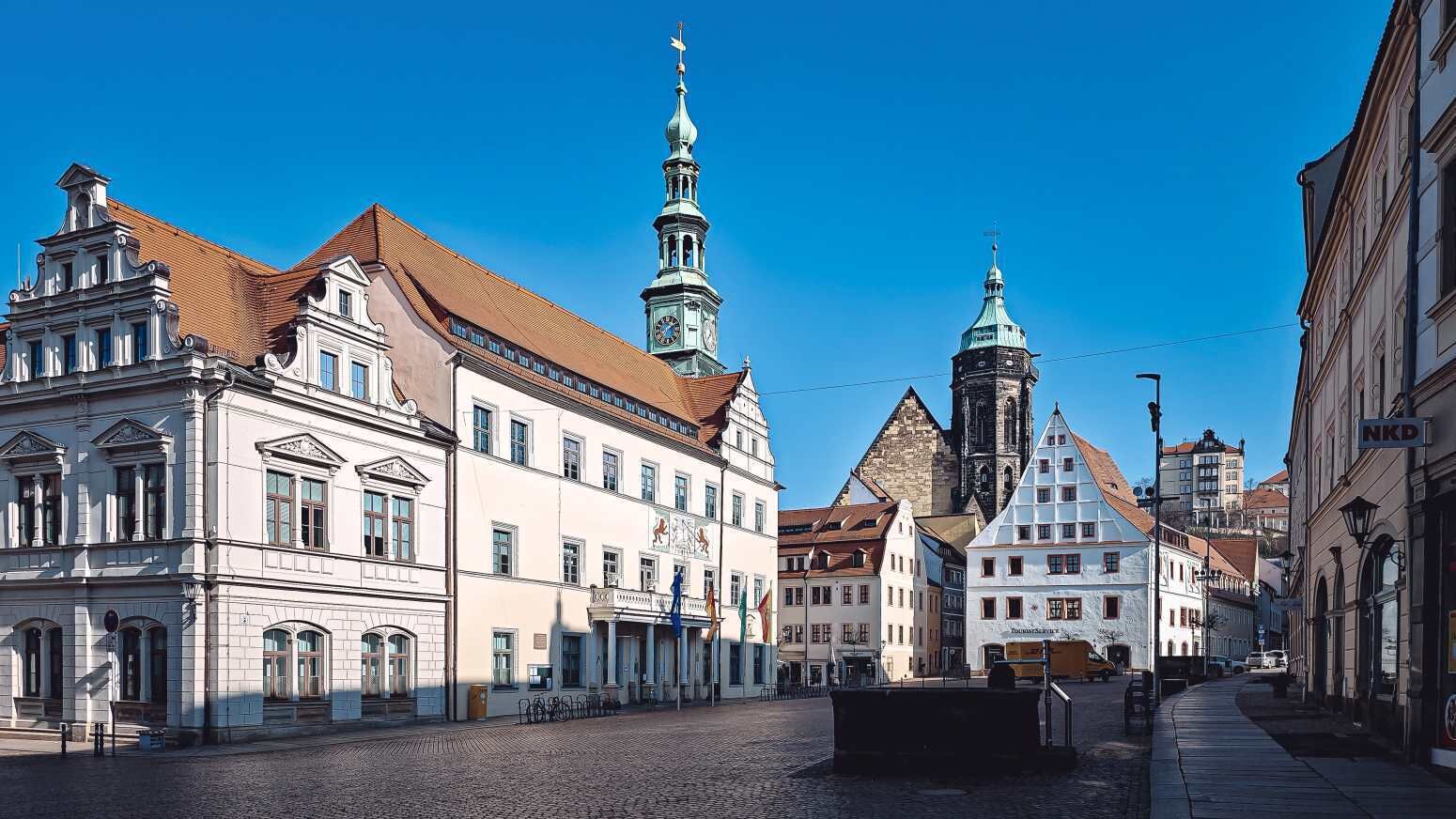 A historic street with traditional European architecture, including a prominent church tower and a building with a clock.