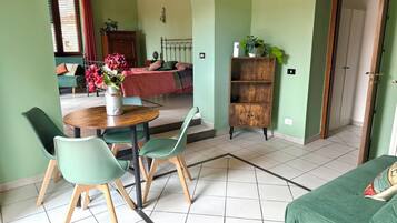 Zona pranzo con un tavolo rotondo in legno, sedie verdi e un divano verde.