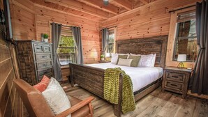 A wooden cabin bedroom with a bed, a chair, a nightstand, and a dresser.