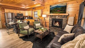 A cozy log cabin interior with a dining area, kitchen, and living room featuring a fireplace.