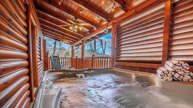 A log cabin with a hot tub, wooden walls, and a ceiling fan.