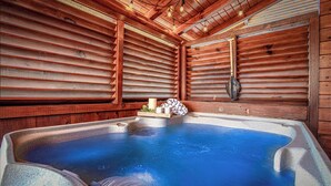 A wooden cabin with a hot tub, wooden walls, and a ceiling with exposed beams.