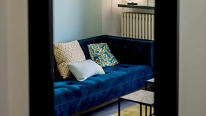 Habitació moderna amb un sofà blau, coixins estampats, una taula petita i una làmpada penjada a la paret.