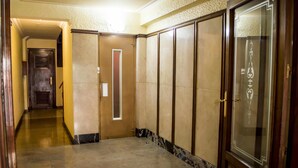 Un passadís amb una porta de fusta, una porta de vidre amb un disseny decoratiu i un paviment de marbre.