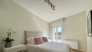 A bedroom with a large bed, a nightstand, a potted orchid, and a window with a view. - Zabella Central Market (Zaragoza)