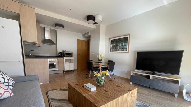A modern living room with a wooden coffee table, a sofa, a TV, and a kitchen in the background. - Zabella Central Market (Zaragoza)