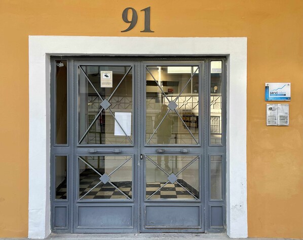 A building entrance with a large number '91' above the door, a glass window with a diamond pattern, and a sign on the wall to the right.