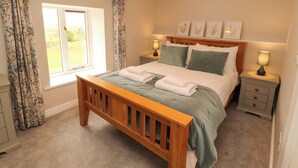 A bedroom with a wooden bed, two bedside tables, a window with curtains, and a wall-mounted lamp.