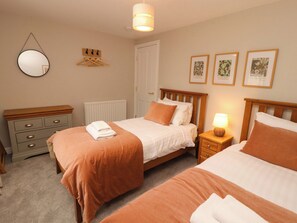 A bedroom with two beds, a dresser, a mirror, a radiator, and framed pictures on the wall. - Swallow's Nest (Keswick)