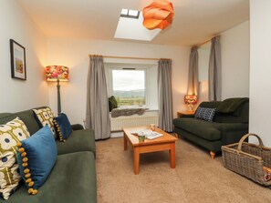 A cozy living room with two green sofas, a wooden coffee table, a floor lamp, and a view of the outdoors through a window. - Swallow's Nest (Keswick)