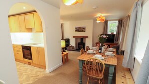 A dining area with a wooden table set for four, a fireplace, and a kitchen in the background.