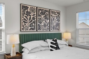 A bedroom with a green upholstered headboard, white bedding, and two bedside lamps.